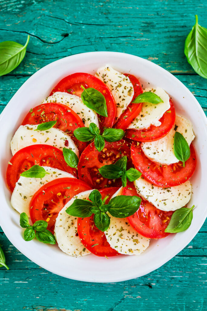 Tomato salad with mozzarella and basil on blue background vertical photo