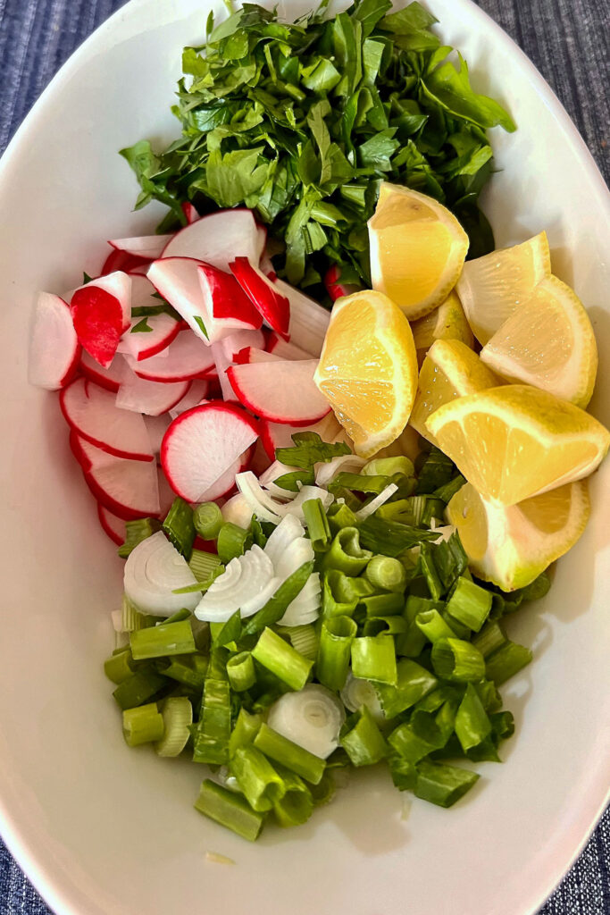 Toppings for easy chicken tacos, radishes, lemon wedges, green onions, cilantro.