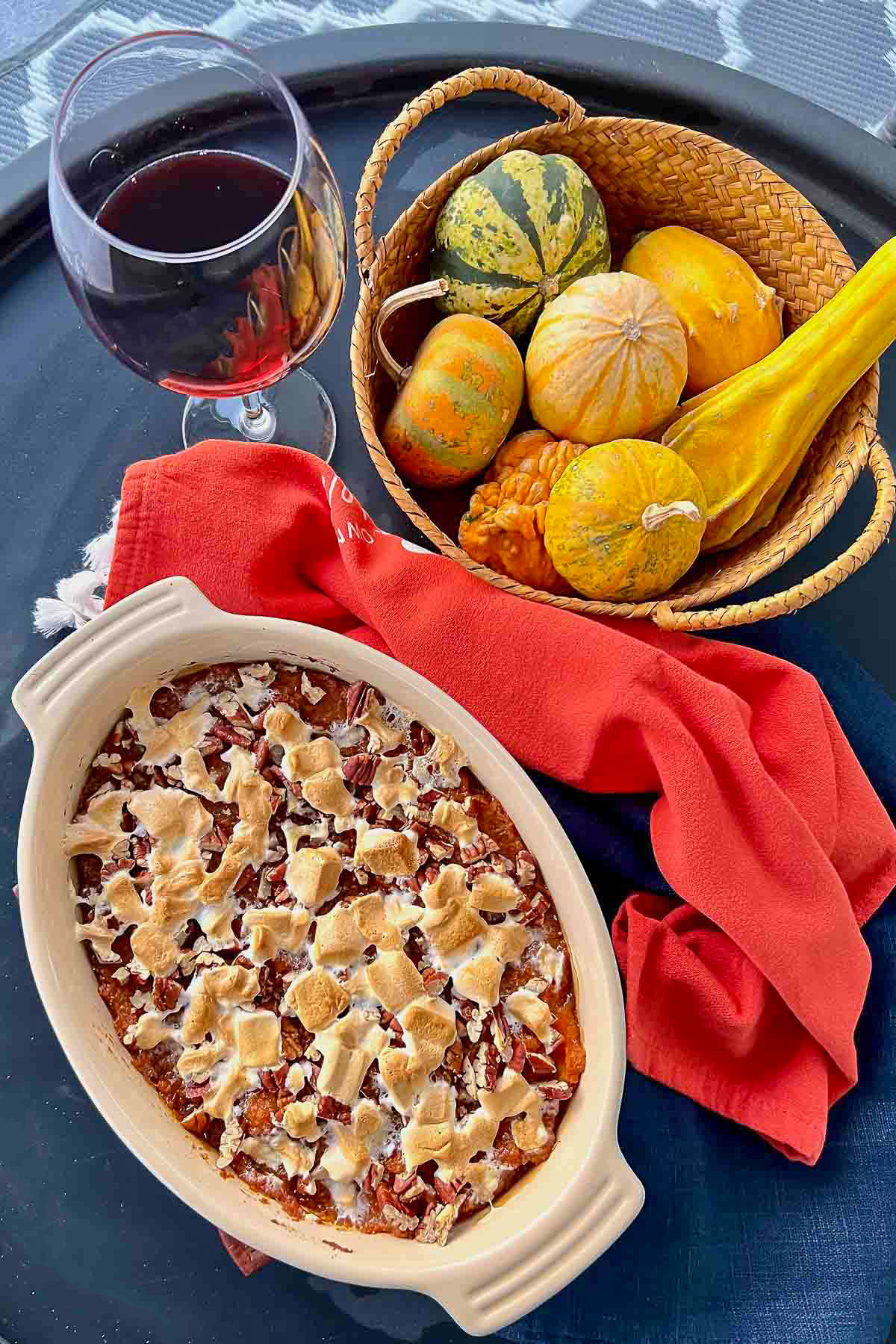 Marshmallow sweet potato casserole on black table with Fall decorations and a glass of red wine in the background.