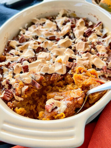 A casserole dish of sweet potato casserole with orange juice with a spoon in the dish and a serving missing.