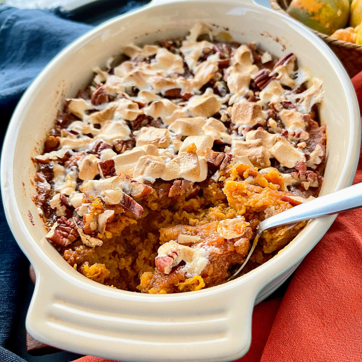 A casserole dish of sweet potato casserole with orange juice with a spoon in the dish and a serving missing.