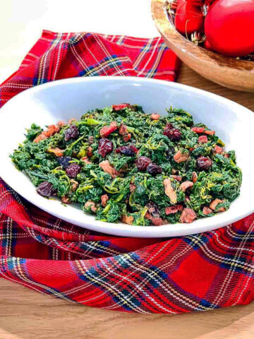 Cooked Spinach With Bacon in a white bowl on Christmas tea towel.
