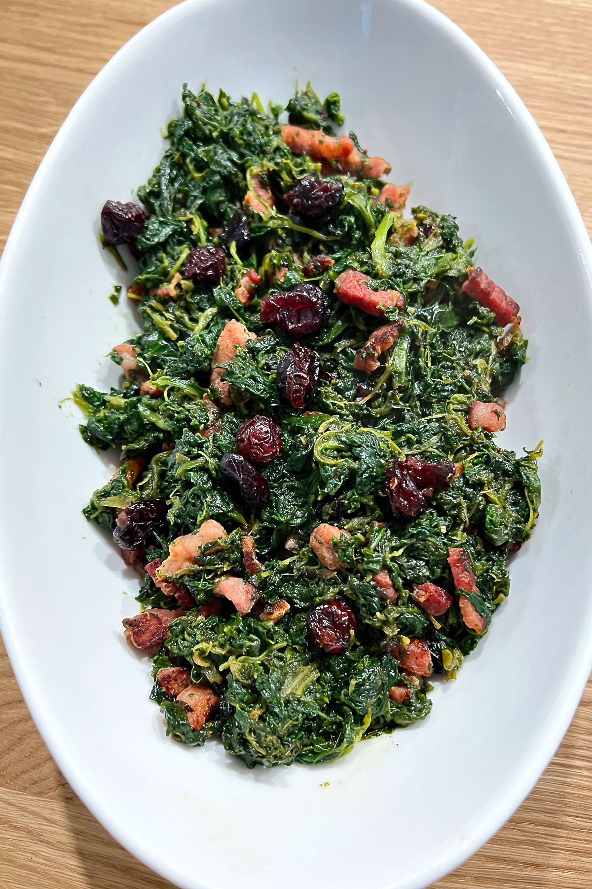 Spinach with bacon in a white bowl.