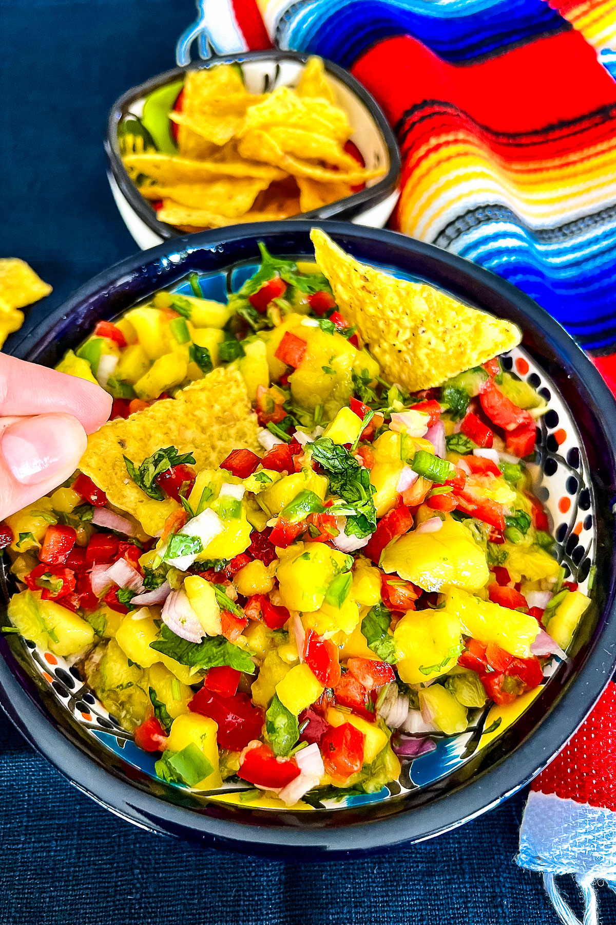 Mango Salsa in a bowl with corn tortilla chips and Mexican towel in the background