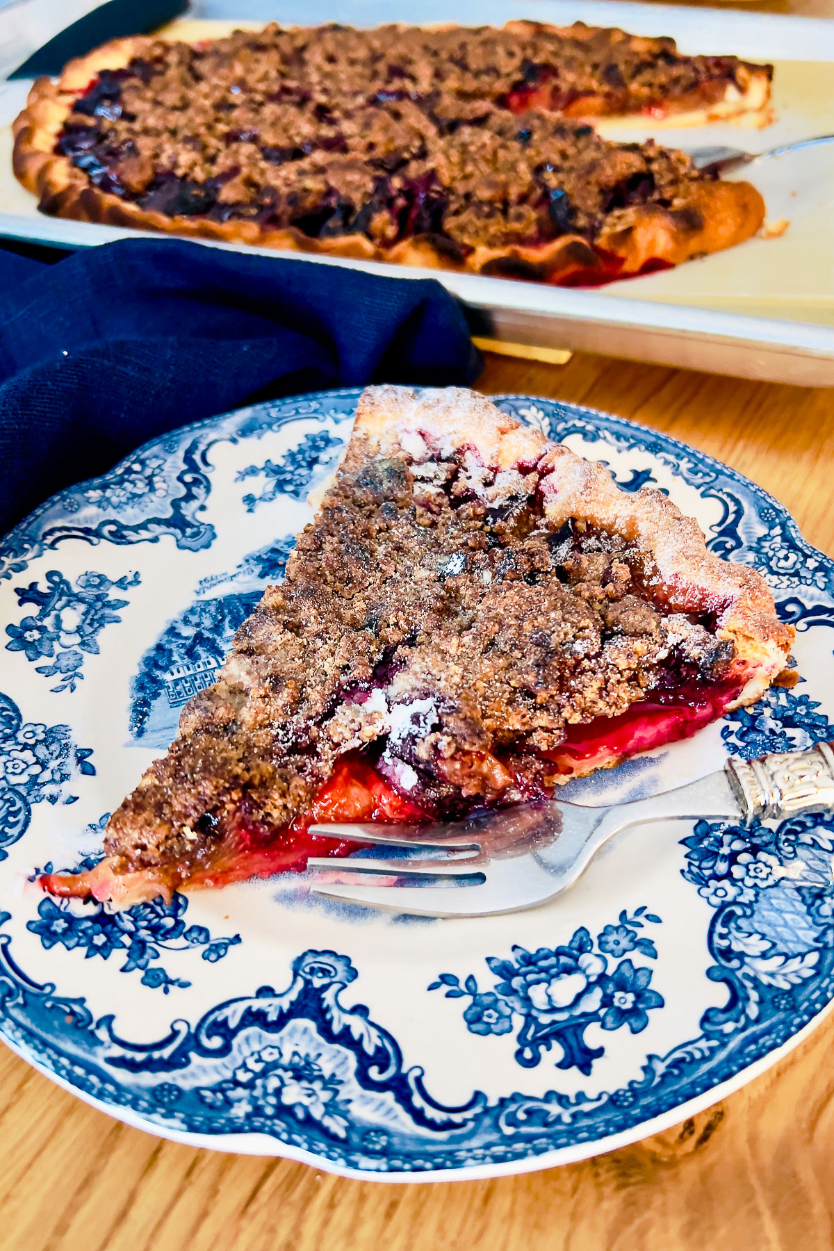 Spiced Plum Crumble Tart on a blue and white plate with baking tray in the background