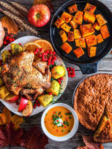 Thanksgiving Food: Roasted Turkey on white plate, roasted vegetables, baked pie with pumpkin decorations in the background.