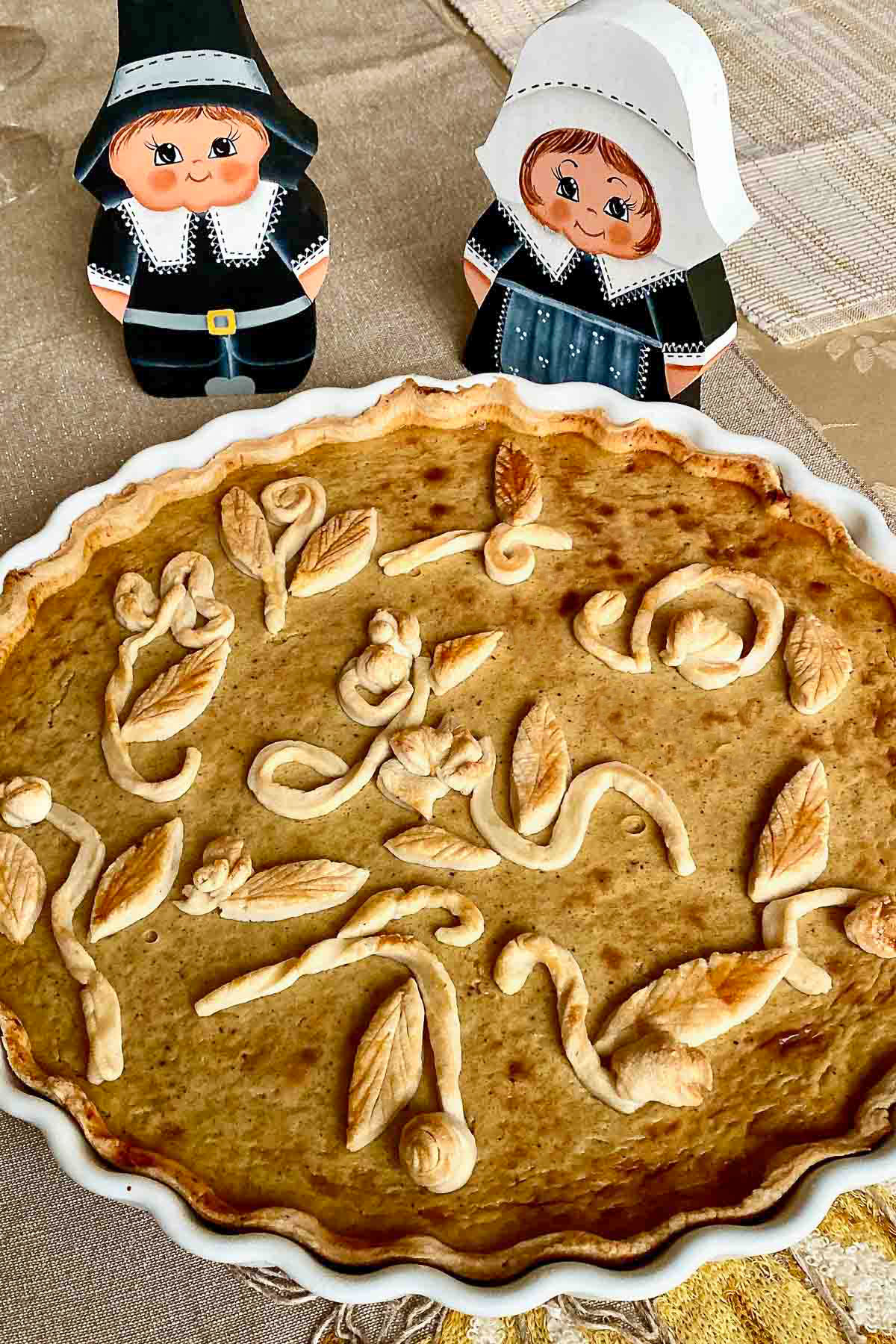 Whiskey flavored pumpkin pie on table with Thanksgiving wooden pilgrims in the background.