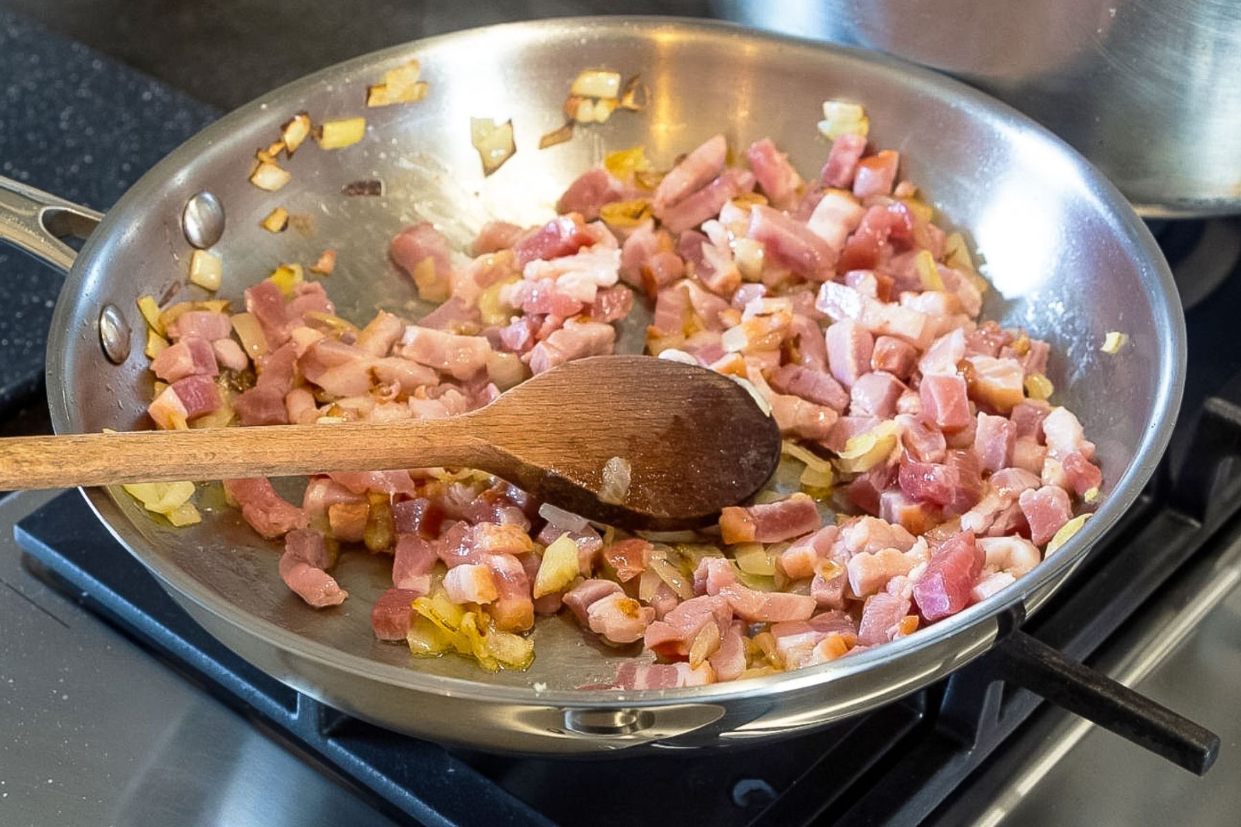 Lardons cooking with onions in a skillet.