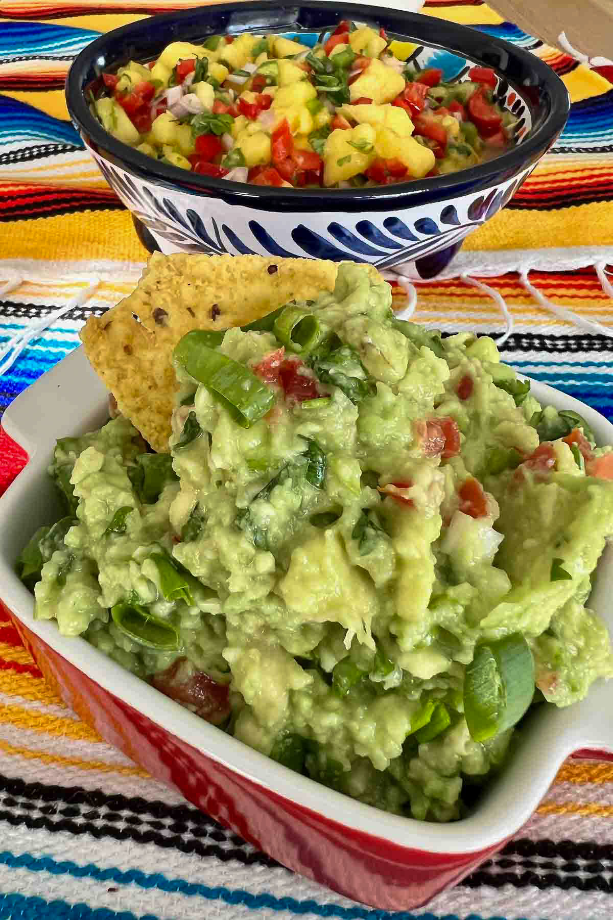Homemade Guacamole in a red bowl with mango salsa in the background.