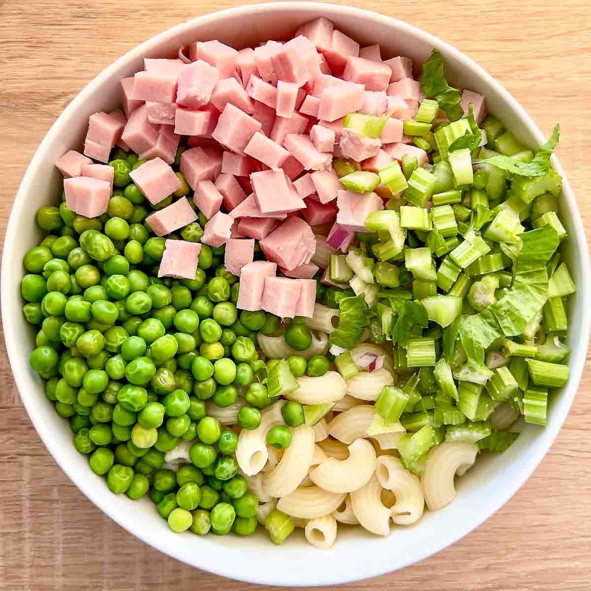 Ingredients for the pasta salad with ham in a salad bowl.