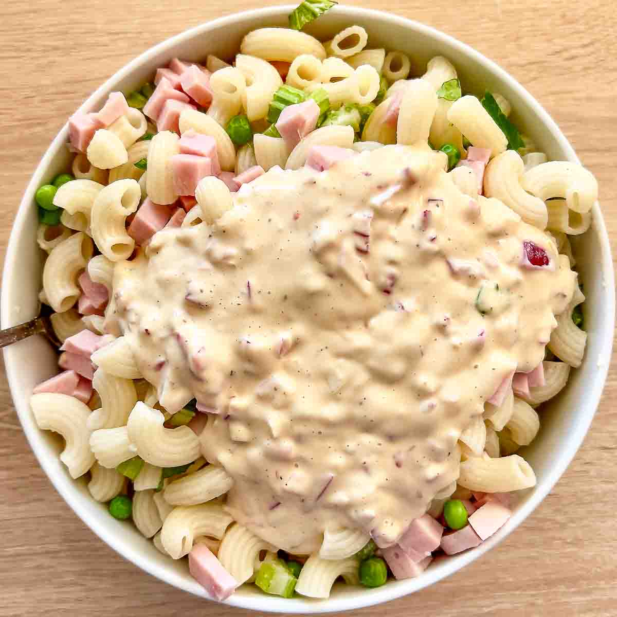 Pouring dressing over the ingredients for the pasta salad with ham.