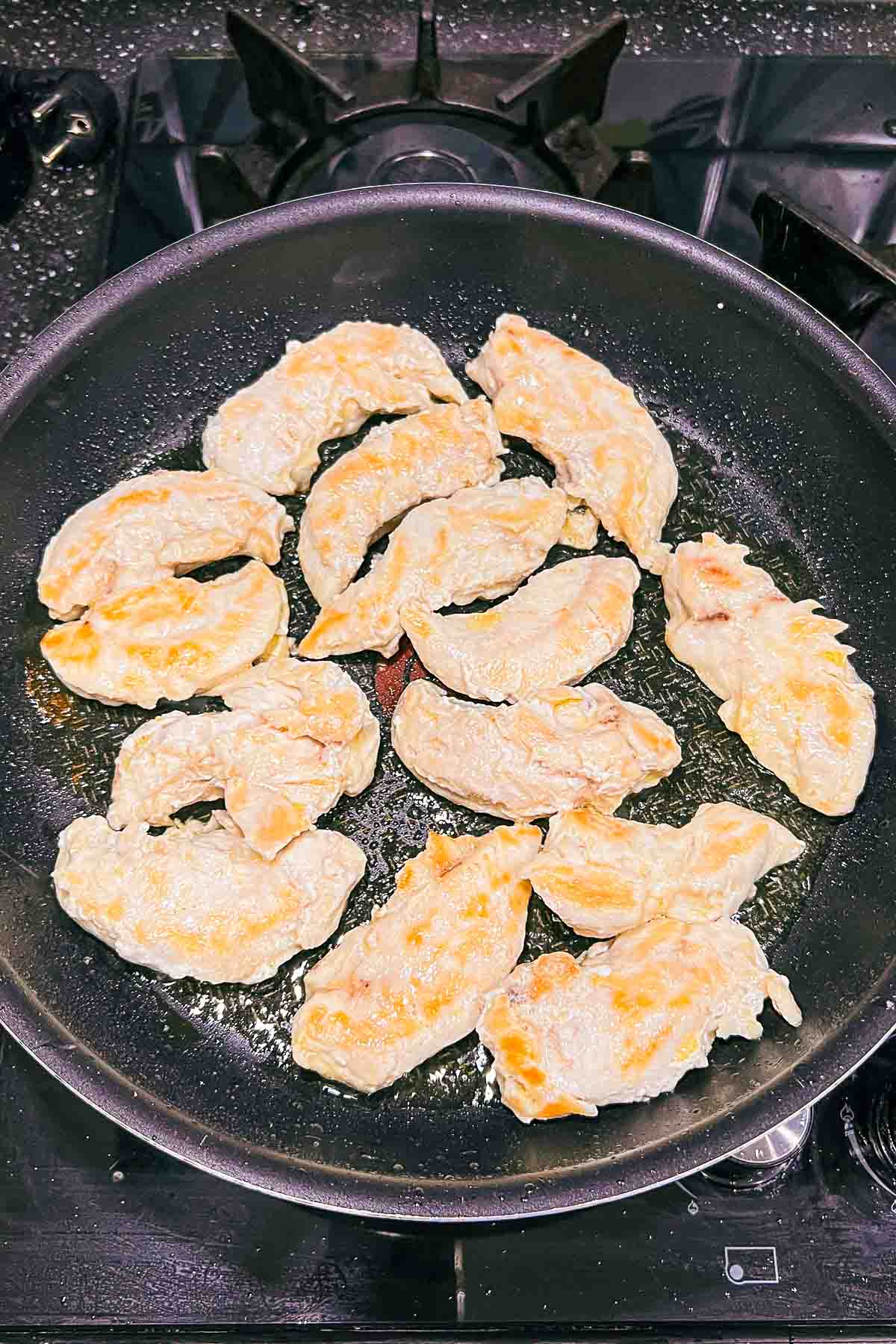 Chicken cutlets cooking in a pan.