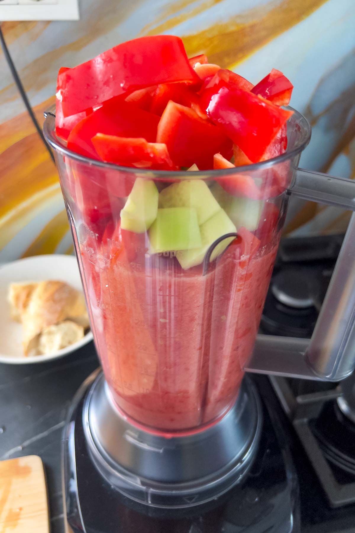 Placing peppers and cucumbers in the blender with tomatoes