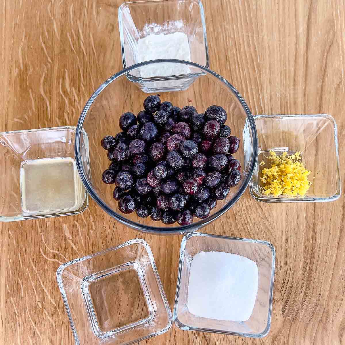 Ingredients for the blueberry layer shown in small bowls: blueberries, sugar, lemon juice and zest, water, flour.